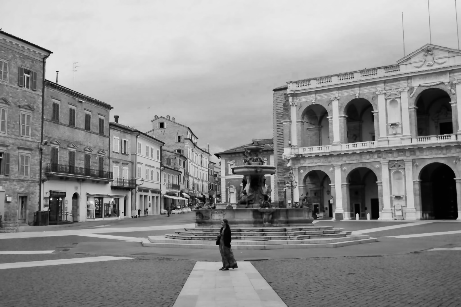 A woman in a long dress stands alone in the centre of a square